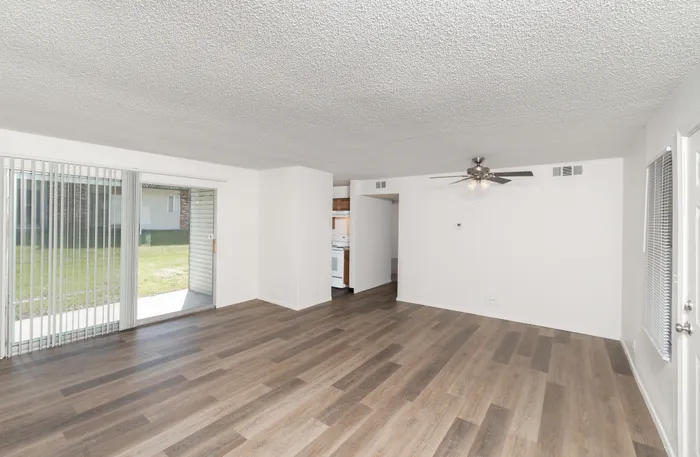 Spacious living room with wood style flooring, ceiling fan, and sliding glass door leading to patio with vertical blinds
