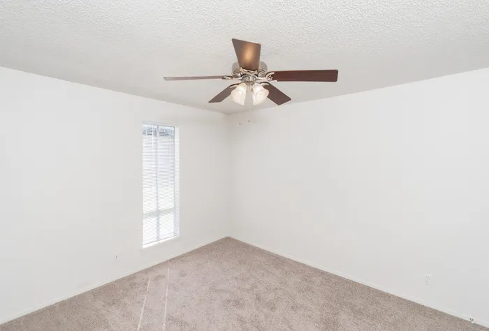 Bright, minimalist room with a modern ceiling fan, cozy carpet, and natural light from a tall window, perfect for a serene living space.
