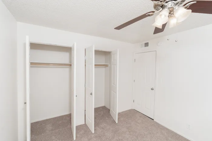 Bedroom featuring dual closets with open doors, carpet flooring, and ceiling fan with light