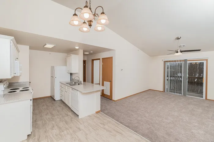 Open concept 1 bedroom apartment at Plainview Park with kitchen island, white cabinets, vinyl flooring, carpeted living room, ceiling fan, and sliding glass door to private balcony