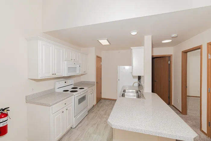 Modern kitchen in Plainview Park 1 bedroom apartment featuring white appliances, electric stove, microwave, double sink, breakfast bar, and ample cabinet storage
