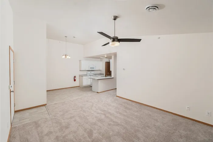 Open living room at Plainview Park 1 bedroom apartment with carpet flooring, ceiling fan, vaulted ceiling, and view into kitchen with breakfast bar