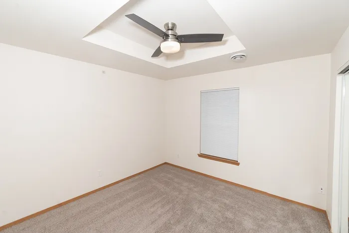 Bedroom in Plainview Park apartment with vaulted ceiling, ceiling fan, carpet flooring, and window with blinds for natural light