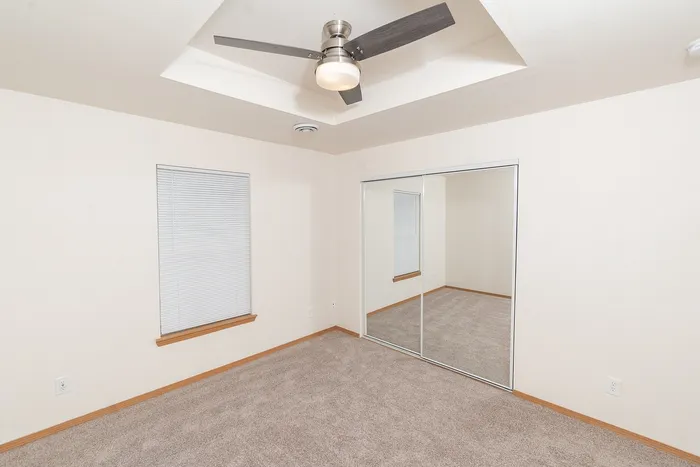 Spacious bedroom with mirrored closet doors, carpet flooring, vaulted ceiling, and ceiling fan at Plainview Park apartments