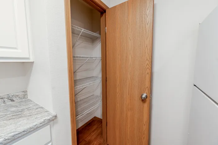 A small pantry with white wire shelves and a wooden door, located next to the kitchen appliances.