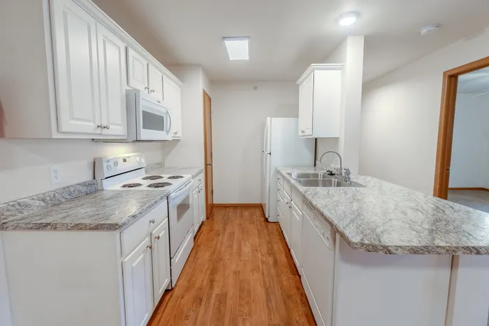 A close-up of the kitchen, showing white cabinetry, granite counters, and stainless steel sink with a double basin.