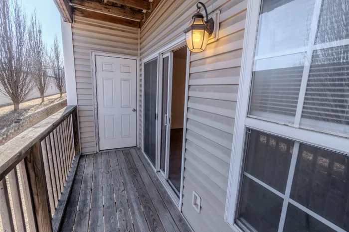 A wooden balcony with a sliding glass door, a white door to a storage room, and a lantern-style exterior light.