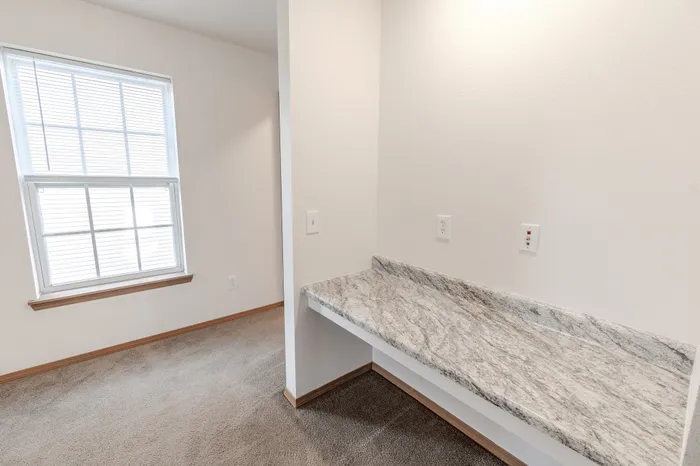 A close-up of a granite vanity area with electrical outlets on the wall, situated next to a window with white blinds.