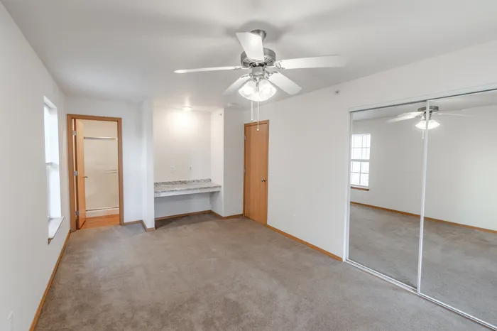 A bedroom with a built-in granite vanity area, beige carpet, and an open doorway leading to a bathroom.