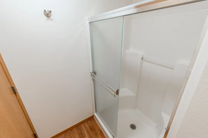 A shower stall with a frosted glass sliding door, white interior, and wooden flooring outside the shower area.
