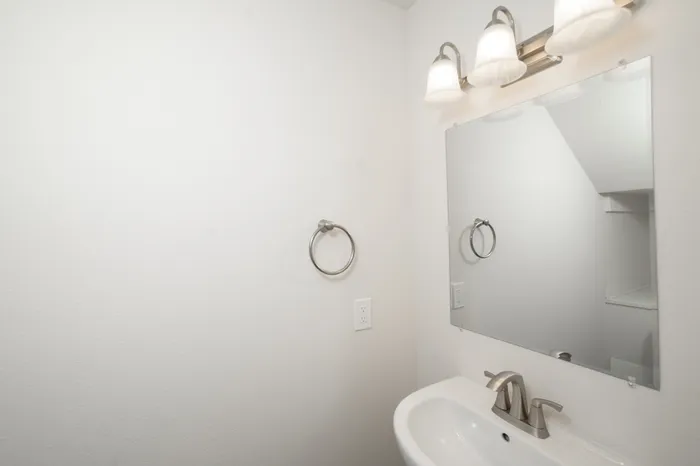 Bathroom vanity with modern lighting, large mirror, brushed nickel fixtures, and neutral walls in Dryden Place Townhomes