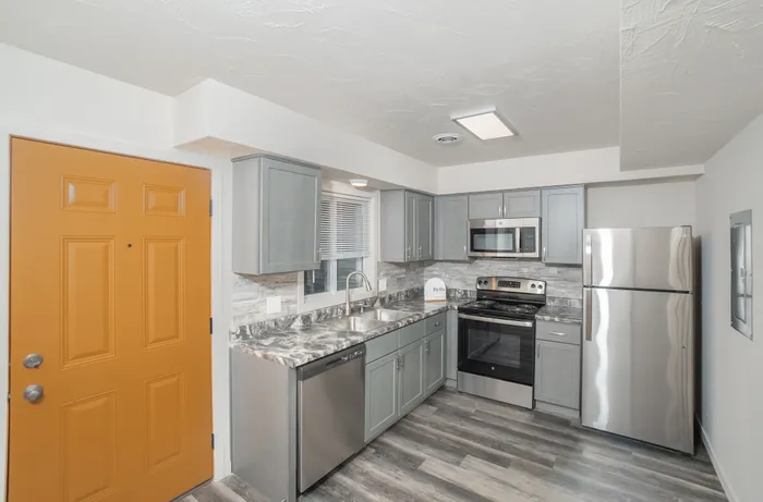 Modern kitchen with gray cabinetry, stainless steel appliances, double sink, and marble look countertops at Dryden Place Townhomes