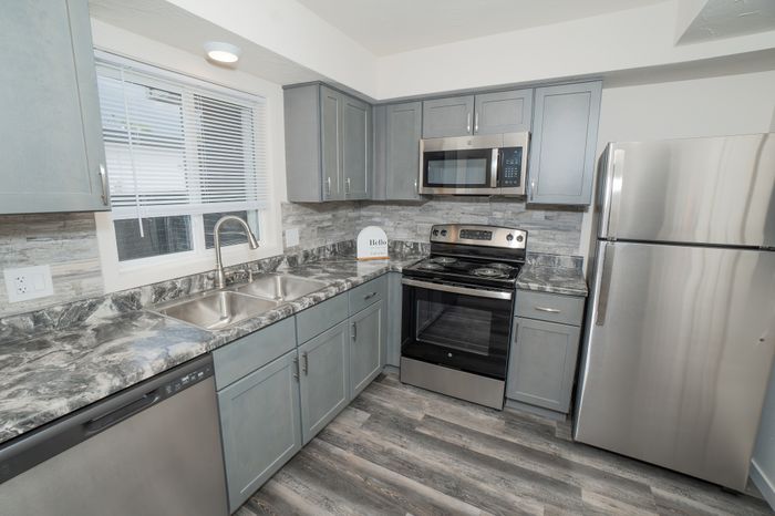 Updated kitchen featuring stainless steel refrigerator, electric range, microwave, gray cabinets, and wood style flooring at Dryden Place Townhomes