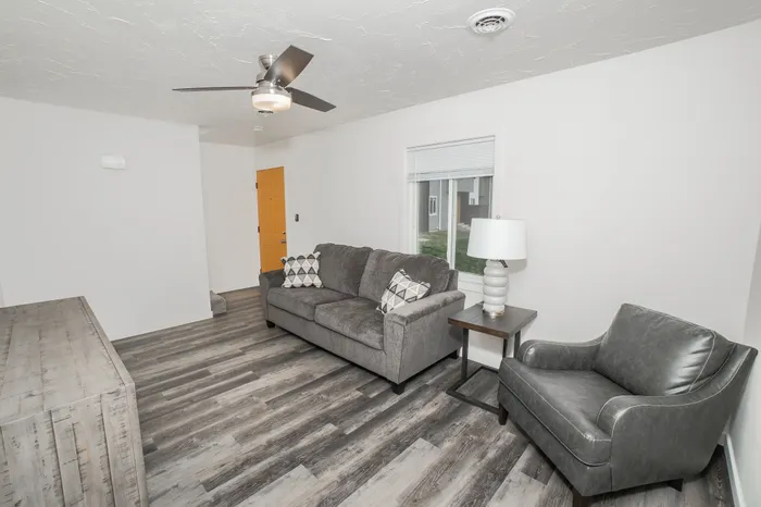 Living room with wood style flooring, large window, ceiling fan, and staged seating area in Dryden Place Townhomes