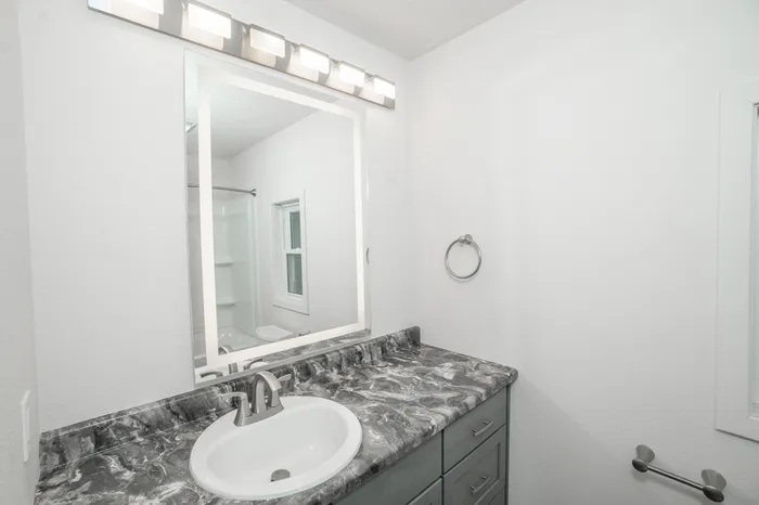Bathroom vanity with marble look countertop, modern lighting, large mirror, and gray cabinetry in Dryden Place Townhomes