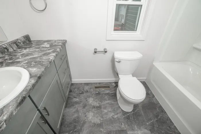 Bathroom with vanity, toilet, window for natural light, and marble look flooring in Dryden Place Townhomes