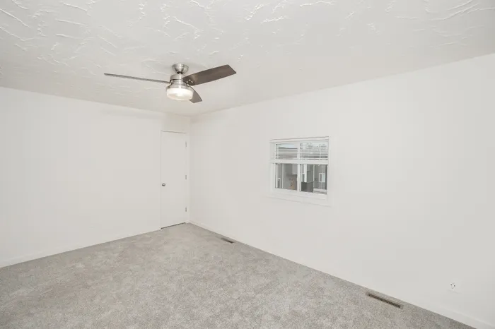 Spacious bedroom with soft carpet, ceiling fan, and natural light in Dryden Place Townhomes