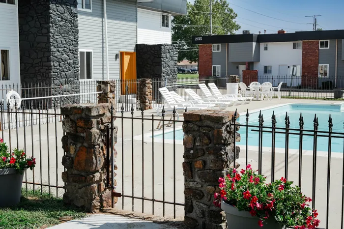 Inviting apartment community with a sparkling outdoor pool, surrounded by comfortable lounge chairs and vibrant flower arrangements, perfect for relaxation and enjoyment.