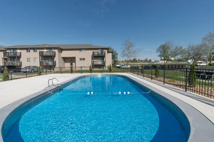 Inviting outdoor pool with crystal-clear water, surrounded by modern apartment buildings and well-maintained landscaping under a bright blue sky.