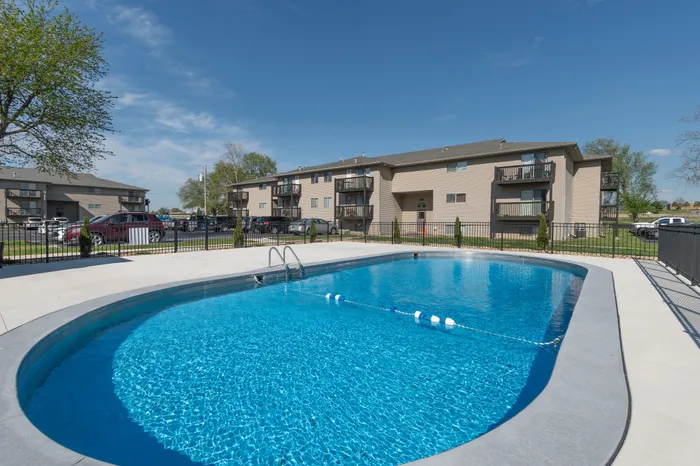 Charming apartment complex featuring inviting outdoor pool with pristine clear water, surrounded by modern, well-maintained buildings under a bright blue sky.