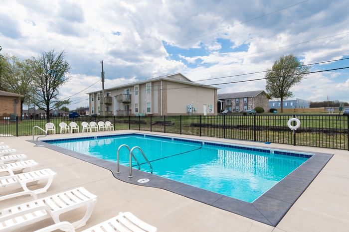Charming apartment complex with a sparkling outdoor swimming pool surrounded by inviting lounge chairs, ideal for relaxation and leisure.