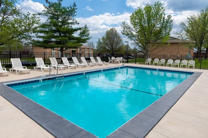Inviting outdoor swimming pool with bright turquoise water, surrounded by comfortable lounge chairs and lush green trees in a serene residential setting.
