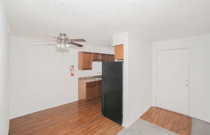 Open concept living and dining area at Rosewood Village Apartments with wood style flooring, neutral paint tones, ceiling fans, and a connected galley kitchen with dark appliances and updated cabinetry.