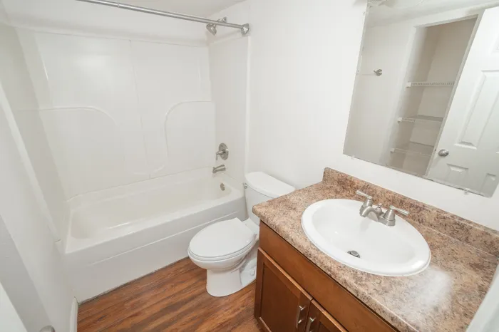 Updated bathroom at Rosewood Village Apartments featuring a full bathtub and shower combination, wood style flooring, modern vanity cabinetry, brushed nickel fixtures, and neutral finishes.