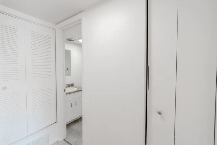 Hallway view showing entry to the bathroom and louvered closet doors for extra storage.