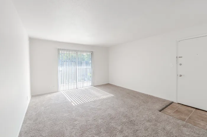 Bright living area in the Classic 1 Bedroom at Rosewood Village, featuring sliding glass doors and soft carpet flooring.