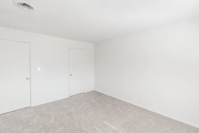 Bedroom interior with neutral carpet, two closed white doors, and overhead vent, providing a clean and simple layout.