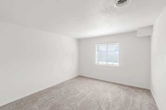 Spacious bedroom in the Classic 1 Bedroom unit at Rosewood Village with soft carpet and natural light from a large window.