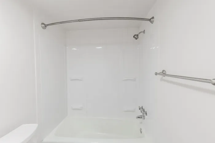 Close-up of the bathtub and shower area with built-in shelving and a curved curtain rod.