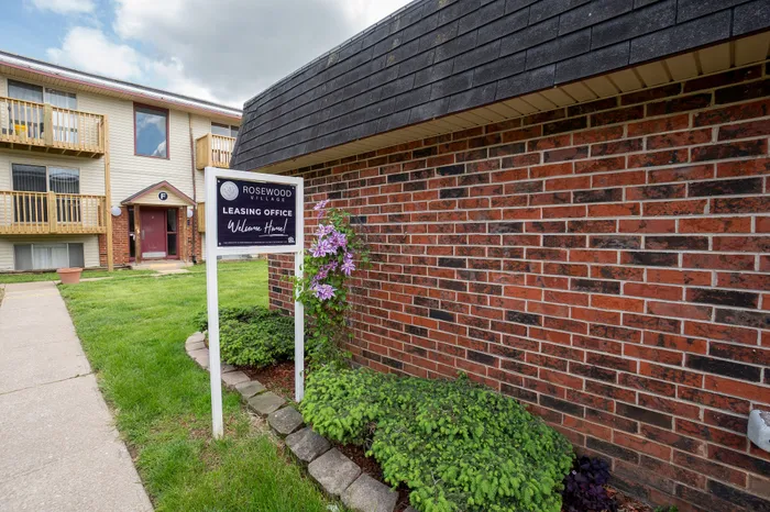 Charming Rosewood Village leasing office with vibrant flowers and inviting brick facade, welcoming potential residents home.