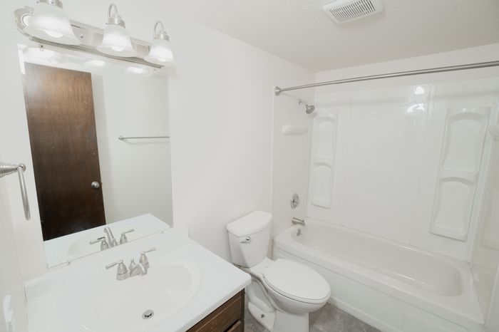 Classic bathroom at El Chaparral Apartments with white vanity, large mirror, bathtub and shower, and neutral flooring.