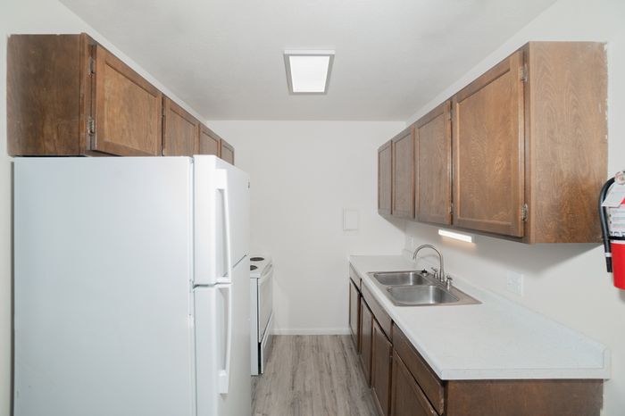Classic kitchen at El Chaparral Apartments with wood cabinets, white appliances, double sink, white countertops, and wood style flooring.