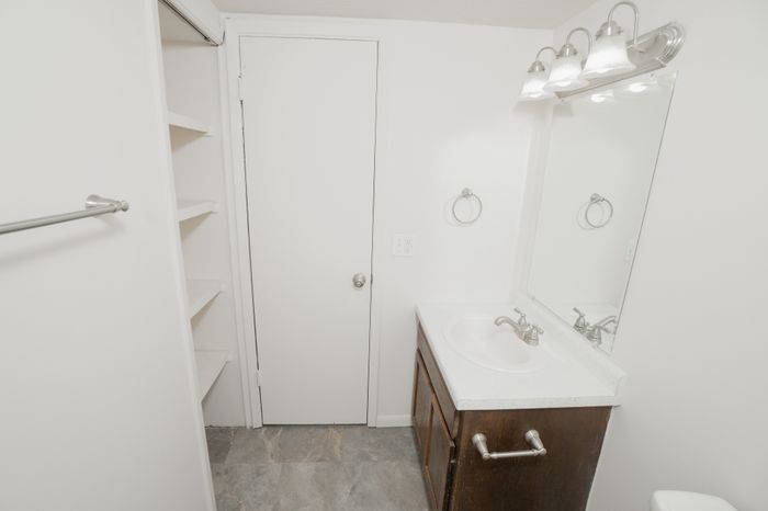 Classic bedroom at El Chaparral Apartments with carpet, ceiling fan, white walls, wood closet door, and view toward the hallway.