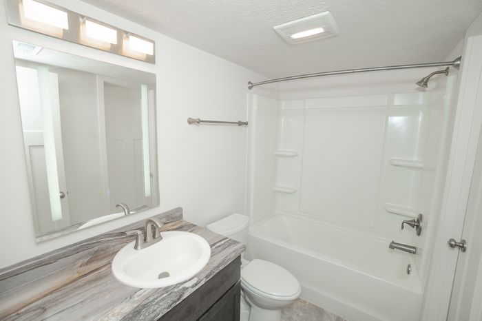 Renovated El Chaparral bathroom with a white bathtub and shower, modern vanity, marble look countertop, large mirror, and brushed nickel fixtures.