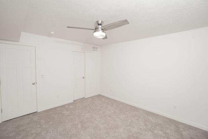 Carpeted bedroom at El Chaparral Apartments with white walls, ceiling fan, closet doors, and neutral finishes.