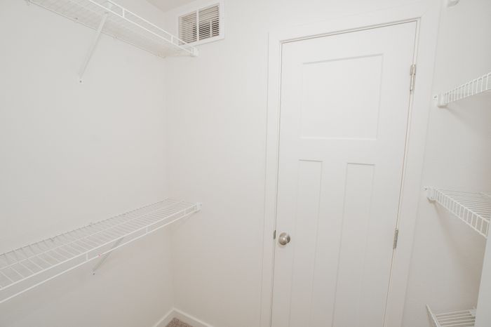 Walk in closet at El Chaparral Apartments with white wire shelving, carpet flooring, and a white paneled door.
