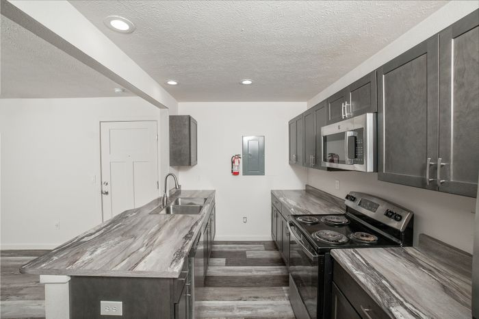 Renovated kitchen at El Chaparral Apartments with dark cabinetry, marble look countertops, stainless steel appliances, and gray wood style flooring.