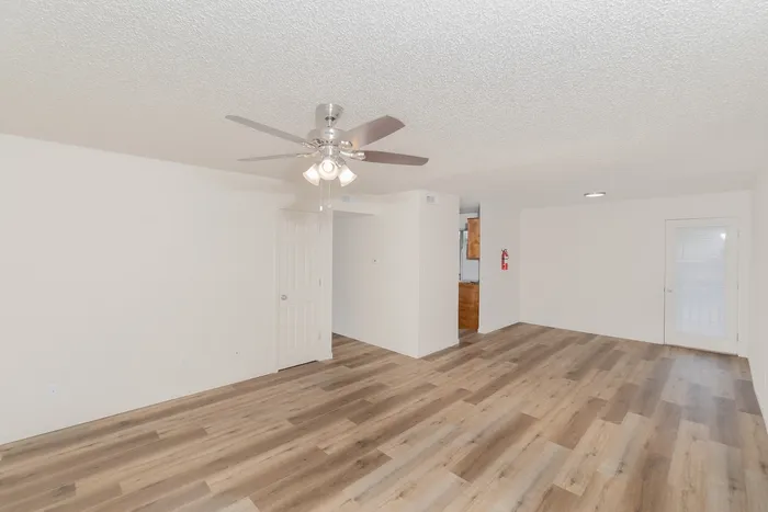 Spacious open concept living and dining area at Quail Ridge East Apartments with modern wood style flooring, neutral paint, ceiling fan, and easy access to the kitchen and patio.