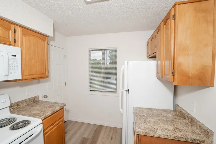 kitchen at Quail Ridge East Apartments with ample cabinet storage, white refrigerator, laminate countertops, natural light from window, and wood style flooring.