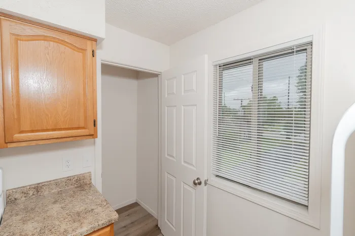 Kitchen storage area at Quail Ridge East Apartments featuring built in pantry shelving, wood cabinetry, laminate countertops, and window with blinds for natural light.