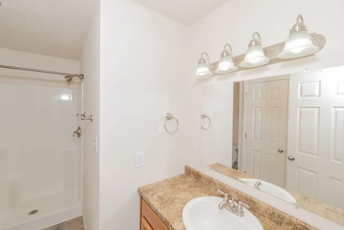 Bathroom vanity at Quail Ridge East Apartments featuring laminate countertops, wood cabinetry, large mirror, modern lighting fixture, and full bathroom access.