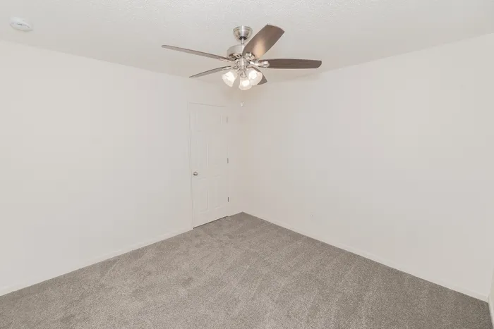 Bright carpeted bedroom interior at Quail Ridge East Apartments featuring neutral paint, ceiling fan, spacious layout, and closet access.