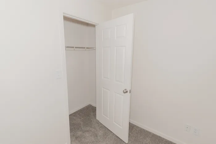 Bedroom closet at Quail Ridge East Apartments with sliding door access, hanging storage space, and soft carpet flooring.
