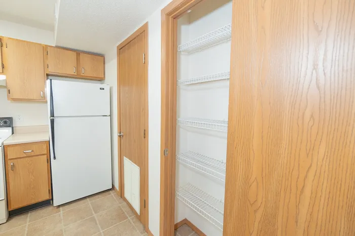 Inviting kitchen with modern wooden cabinetry, spacious pantry shelving, and a sleek refrigerator.