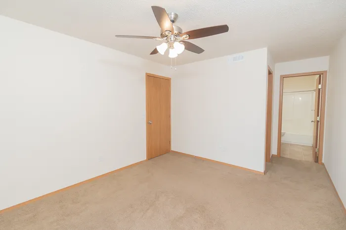 Bright and inviting bedroom with plush carpet, ceiling fan, and an en suite bathroom.