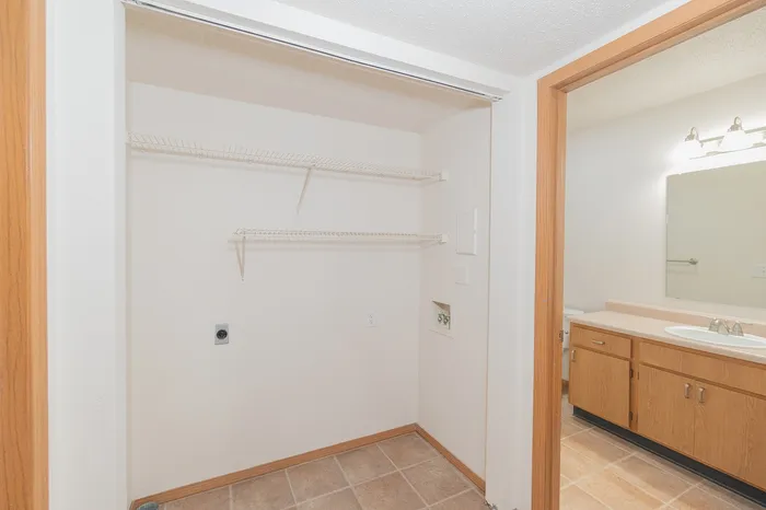 Bright hallway view showcasing a tiled laundry area with wooden shelving, adjacent to a well-lit bathroom with a modern vanity.